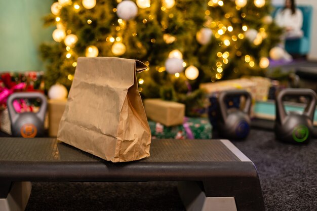 Paquete de entrega con comida sana, peso y pesas en el fondo del árbol de Navidad