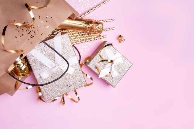 Foto paquete festivo con regalos, champán y cajas de regalo doradas sobre un fondo rosa estilo plano