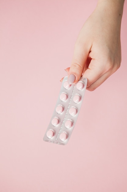 Paquete de pastillas de color rosa en manos de mujer sobre fondo rosa