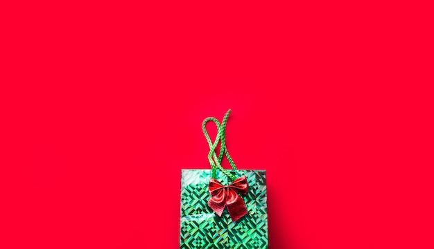 Paquete verde con un regalo y un lazo sobre un fondo rojo con copyspace. Un regalo para año nuevo, Navidad, cumpleaños, aniversario, fiesta. Compras