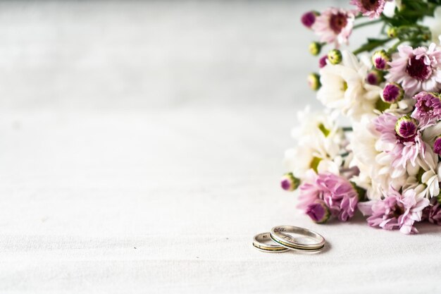 Par de anillos de boda sobre una superficie blanca con hermosas flores blancas y púrpuras en el borde. Concepto de compromiso y amor. Copia espacio