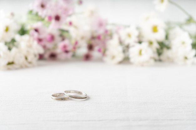 Par de anillos de boda sobre una superficie blanca con hermosas flores blancas y púrpuras fuera de foco en el fondo. Concepto de compromiso y amor.