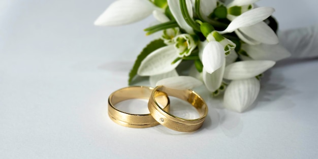 Un par de anillos de bodas de oro con uno de ellos descansando sobre un fondo blanco.