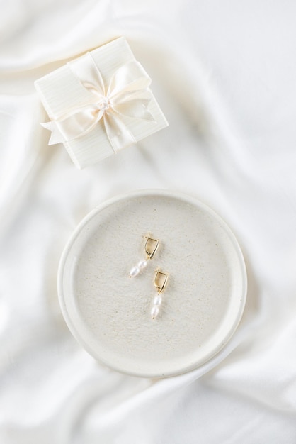 Un par de aretes de perlas naturales con una caja de regalo sobre un fondo claro