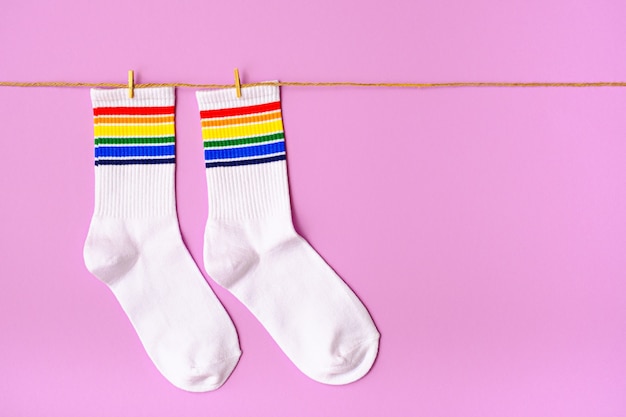 Par de calcetines blancos con ribete de arco iris sobre fondo rosa, espacio de copia