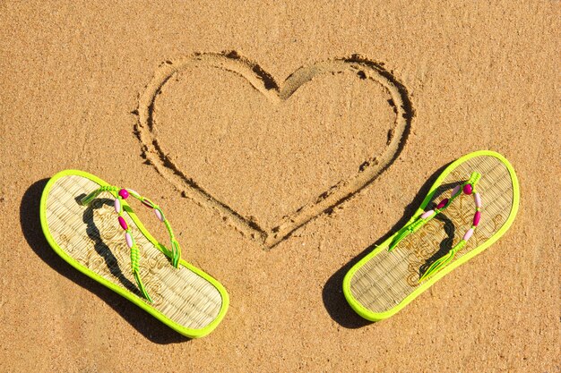 Un par de chanclas en la arena con forma de corazón.