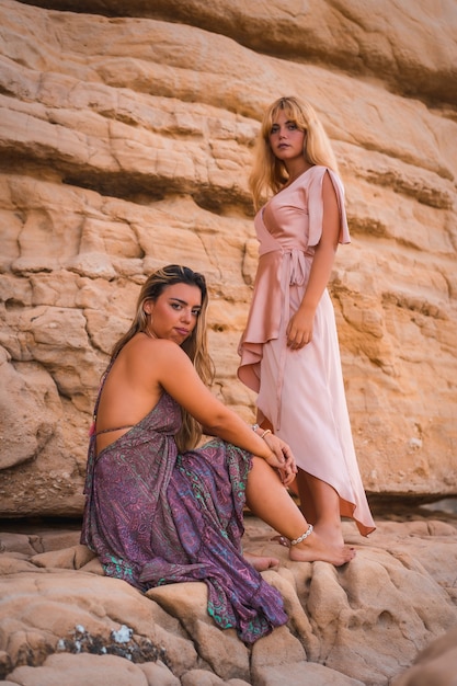 Un par de chicas caucásicas sentadas en la playa con vestidos muy bonitos disfrutando del verano