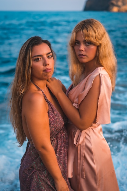 Un par de chicas caucásicas en vestidos rosados, posando el verano en la playa junto al mar