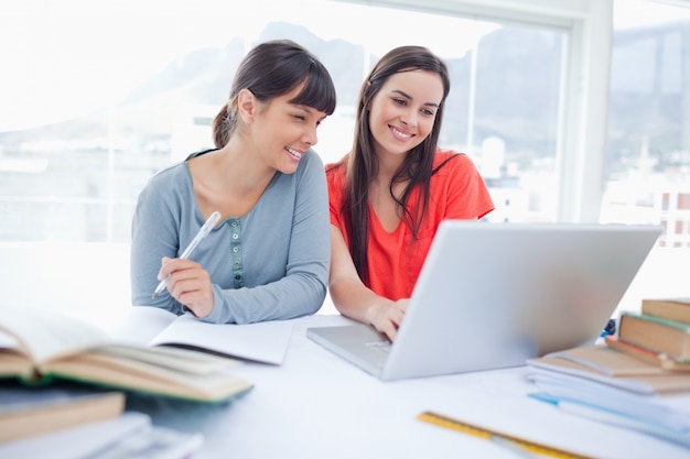 Un par de chicas sentadas juntas mientras trabajan en la computadora portátil