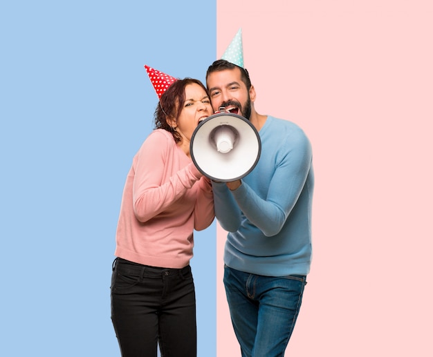 Par, com, chapéus aniversário, e, segurando, um, megafone, ligado, cor-de-rosa azul, fundo