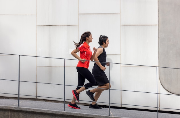 Par de correr haciendo ejercicio afuera en la ciudad en una foto de deporte activo de vida urbana, con edificios en el fondo