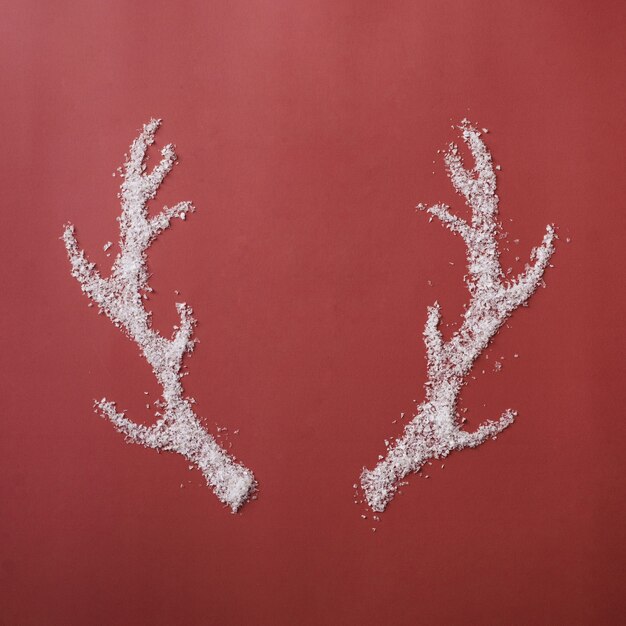 Par de cuernos de reno formados de nieve blanca del invierno sobre un fondo rojo festivo simbólico de la Navidad y la temporada navideña