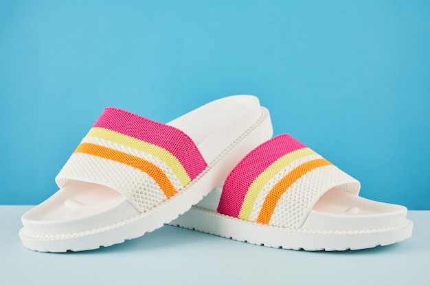 Par de chinelos ou sandálias coloridas de arco-íris multicolorido na parede pastel. Férias na praia e o conceito de verão com espaço de cópia.