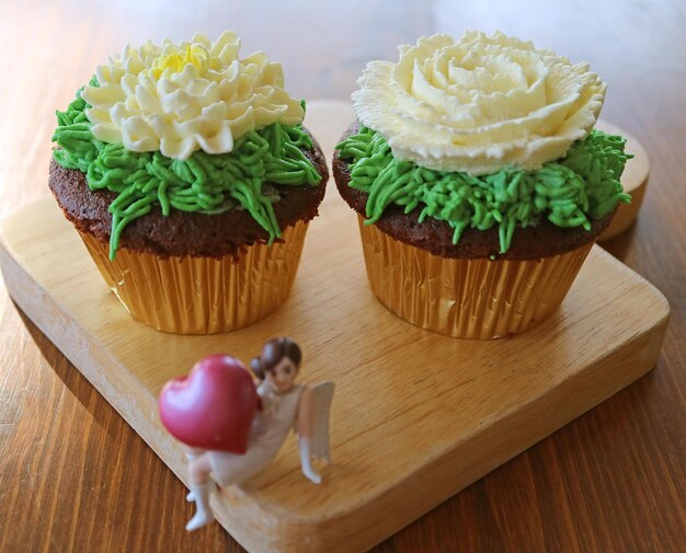 Par de cupcakes de chocolate com chantilly em forma de flor e mini anjo com estatueta de coração grande