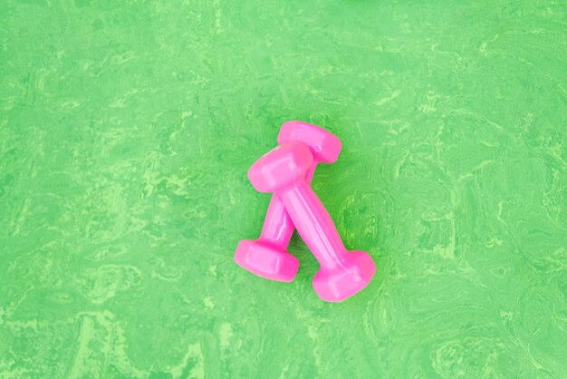 Par de halteres rosa feminino sobre fundo verde. Equipamentos para esportes. Elemento do esporte da aptidão. Vista do topo.