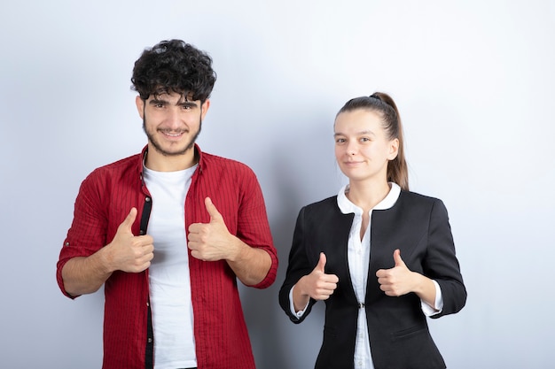 Par de jovens amigos em pé e dando polegares para cima em fundo branco. foto de alta qualidade