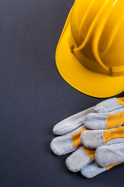 Par de luvas de trabalho protetoras e capacete amarelo em fundo preto