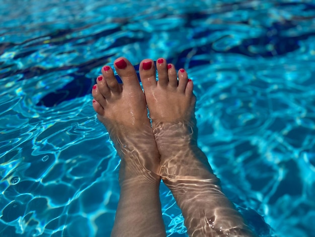 Par de pés de mulher com manicure rosa no fundo da piscina azul