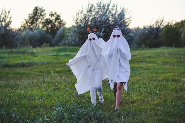 Par de pessoas em fantasias de fantasmas correndo em um campo