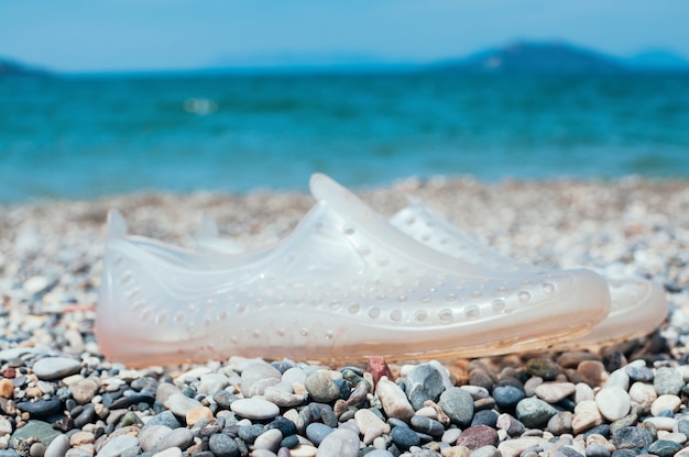 Par de sapatos de natação transparentes na praia de seixos de mármore Conceito de férias de verão