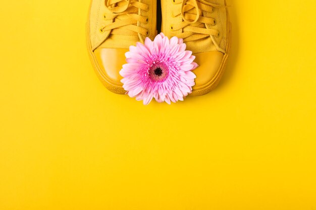 Par de tênis amarelos e flor gerbera rosa em fundo amarelo. Conceito de moda primavera verão.