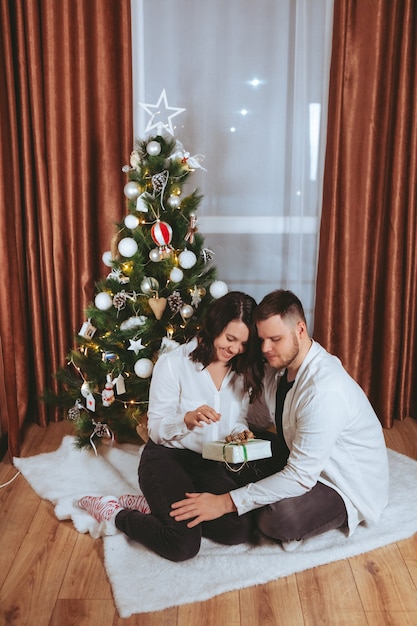 Par disparar delante del árbol de Navidad decorado con tarjeta de regalo de espacio de copia