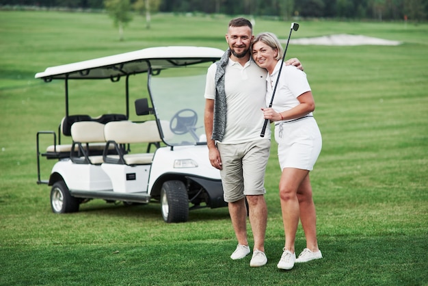 Par de dos golfistas que se quedan en el césped verde con el carro detrás de ellos.