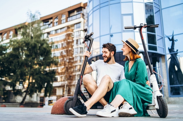 Foto un par de dos personas atractivas se están enfriando cerca del edificio de vidrio con sus electro scooters. hombre y mujer disfrutan de vacaciones