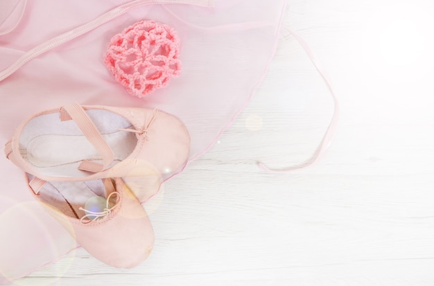 Par de dos zapatillas de ballet rosa satinado y tutú sobre superficie de madera blanca