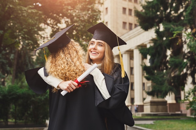 Un par de estudiantes abrazándose en su graduación. Concepto de educación, cualificación y vestido.