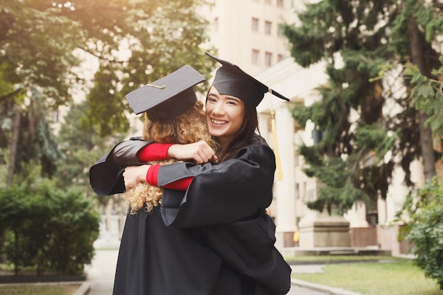 Un par de estudiantes abrazándose en su graduación. Concepto de educación, cualificación y vestido.