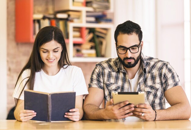 Un par de estudiantes obtienen conocimientos de libros y tabletas sentados en una habitación moderna y elegante con estanterías en el fondo