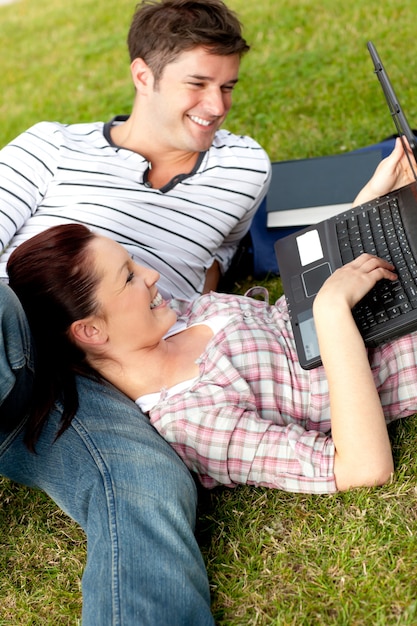 Par de estudiantes positivos usando una computadora portátil tumbado en la hierba