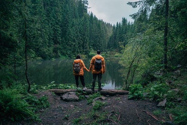 Un par de excursionistas con impermeable amarillo mirando el lago de montaña