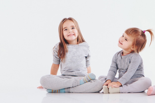 Par de gemelos sentados en el suelo aislado sobre un fondo blanco niños en ropa gris