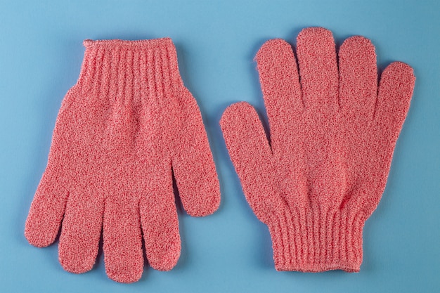 Un par de guantes de masaje rosa para ducharse sobre fondo azul.