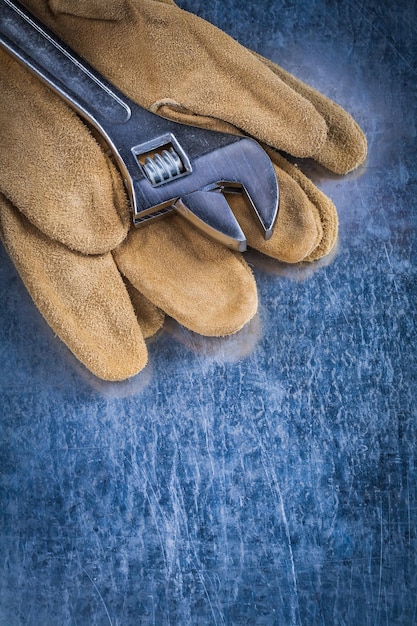 Par de guantes protectores de cuero con llave ajustable de metal sobre el concepto de construcción de fondo metálico rayado