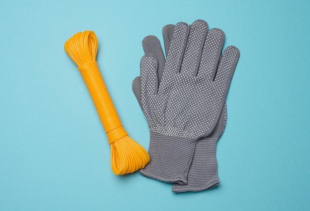 Un par de guantes de trabajo protectores textiles grises y una cuerda naranja en una vista superior de fondo azul