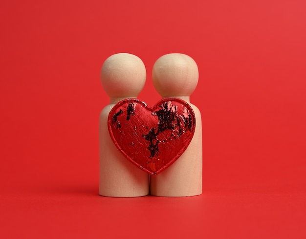 Par de hombres de madera de los novios, entre ellos un corazón rojo, fondo rojo, el concepto de amor y relaciones