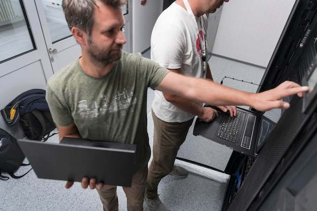 Un par de ingenieros de servidores cooperan en centros de datos de alta tecnología. El equipo de técnicos actualiza el rendimiento del sistema de inspección de hardware en la sala de servidores de supercomputadoras o en la granja minera de criptomonedas.