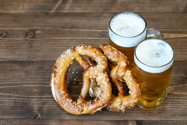 Un par de jarras con cerveza ligera y pretzels en madera