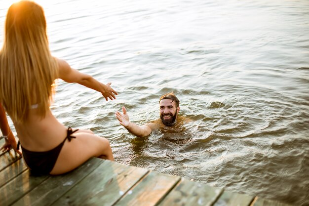 Par jovem, desfrutando, enquanto, mulher senta-se, ligado, cais, e, homem, natação, em, a, lago