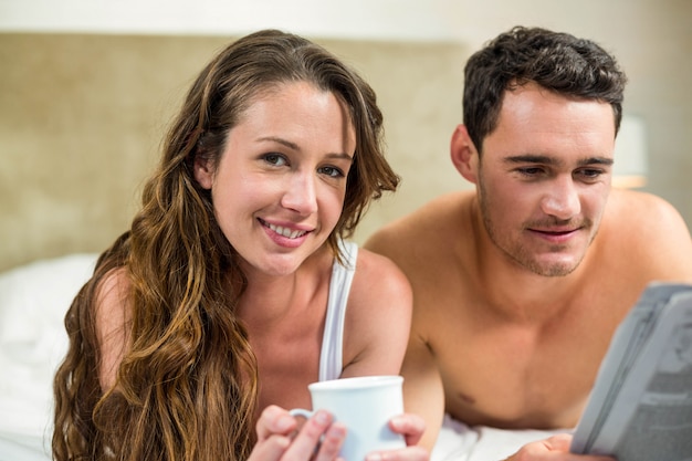 Par jovem, relaxante, e, lendo um jornal, cama