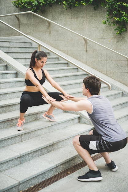 Par de joven guapo caucásica deportiva hombre y mujer ayudarse unos a otros a hacer sentadillas