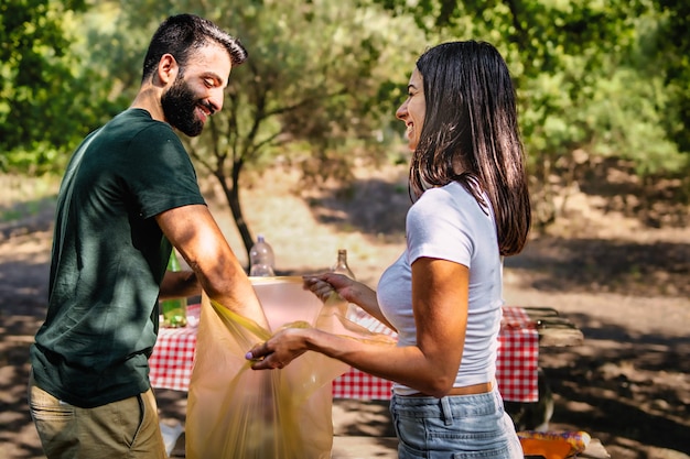 Un par de jóvenes recogiendo basura después del picnic en el parque en una bolsa de plástico