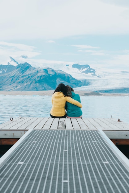 Un par de jóvenes viajeras sentadas en los muelles relajándose y pensando frente a los glaciares de Jokulsarlon en Islandia Copiar espacio Vive el amor de tus sueños al estilo de un viaje por carretera en Islandia