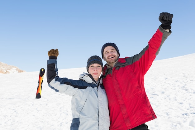 Par levantando las manos con el tablero de esquí en la nieve en el fondo