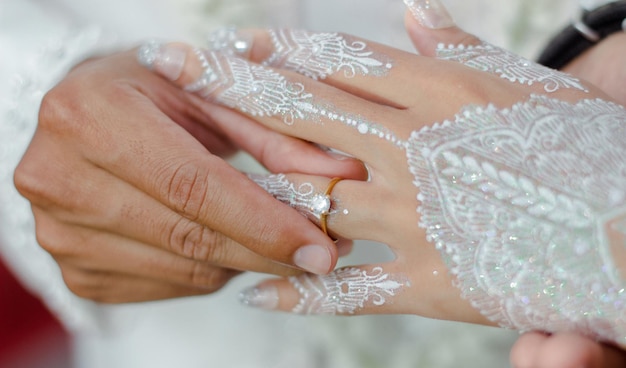 Un par de manos están cubiertas de henna y henna blanca el día de su boda.