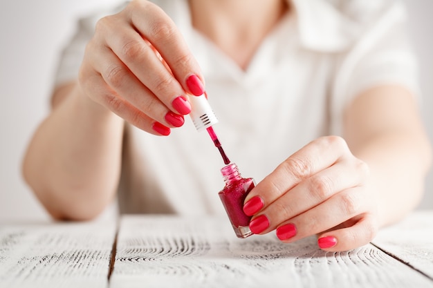 Par de manos femeninas abriendo botella de esmalte de uñas