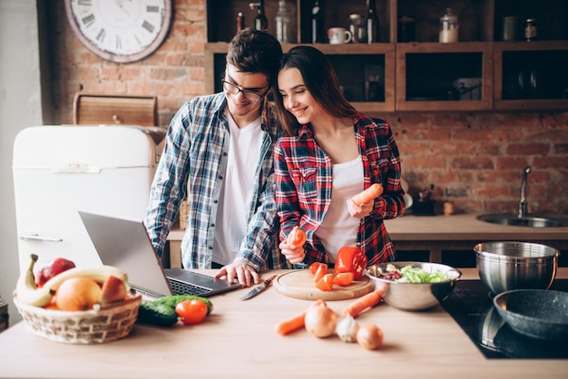 Par mira una receta en la computadora portátil, cocinar ensaladas